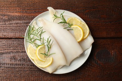 Photo of Pieces of raw squids with rosemary and lemon on wooden table, top view