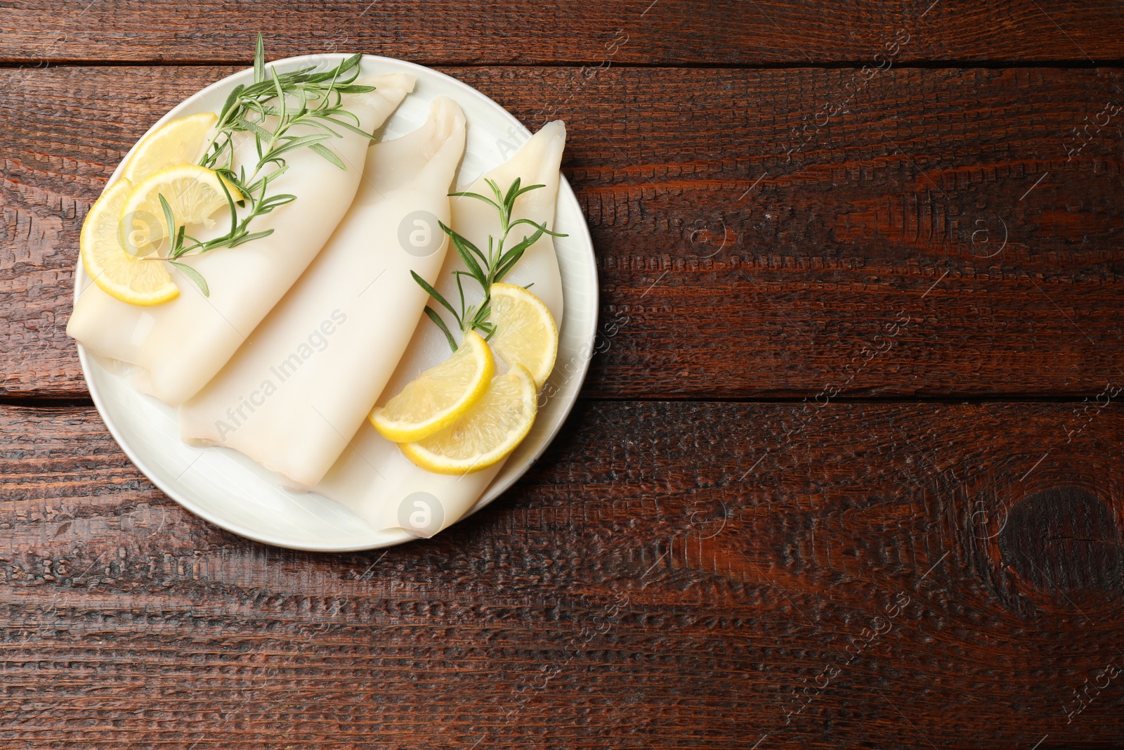 Photo of Pieces of raw squids with rosemary and lemon on wooden table, top view. Space for text
