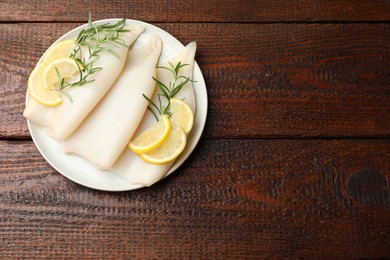 Photo of Pieces of raw squids with rosemary and lemon on wooden table, top view. Space for text