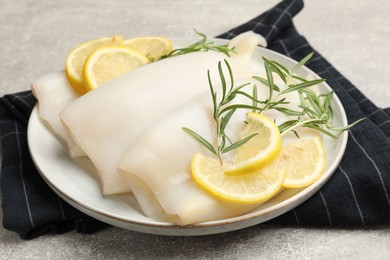 Photo of Pieces of raw squids with rosemary and lemon on grey textured table, closeup