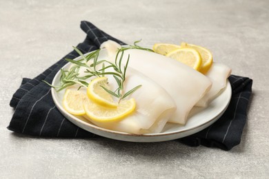 Photo of Pieces of raw squids with rosemary and lemon on grey textured table, closeup