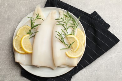 Photo of Pieces of raw squids with rosemary and lemon on grey textured table, top view