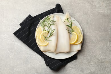 Photo of Pieces of raw squids with rosemary and lemon on grey textured table, top view
