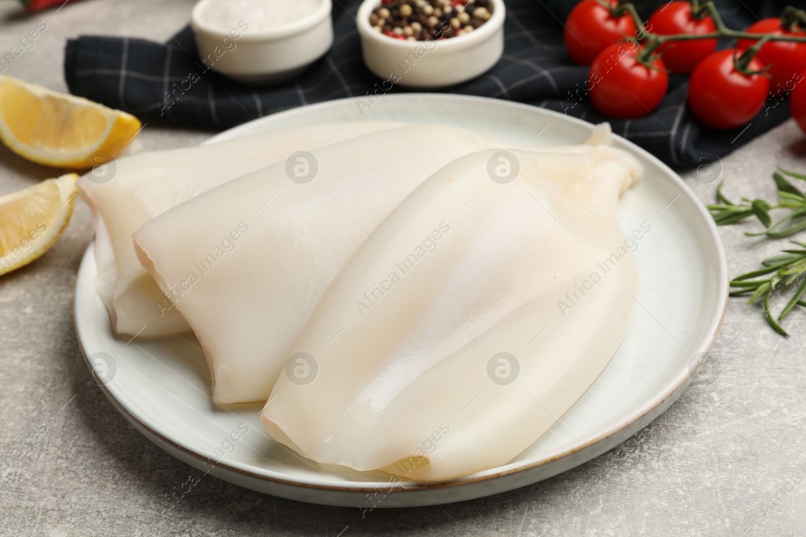 Photo of Pieces of raw squids and products on grey textured table, closeup