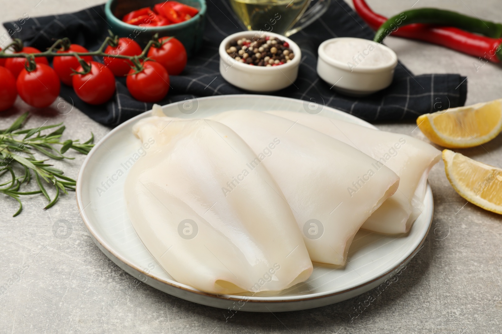 Photo of Pieces of raw squids and products on grey textured table, closeup