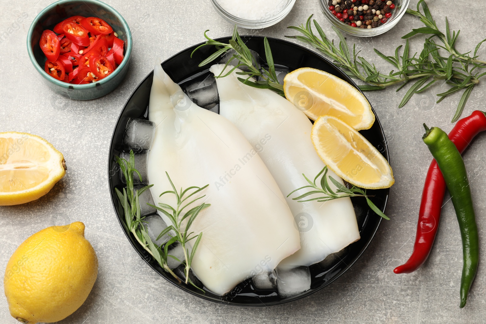 Pieces of raw squids with ice cubes, lemon, rosemary, spices and products on grey textured table, flat lay Photo of Pieces of raw squids with ice cubes, lemon, rosemary, spices and products on grey textured table, flat lay