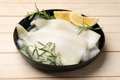 Photo of Pieces of raw squids with ice cubes, lemon and rosemary on light wooden table, closeup