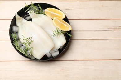 Photo of Pieces of raw squids with ice cubes, lemon and rosemary on light wooden table, top view. Space for text