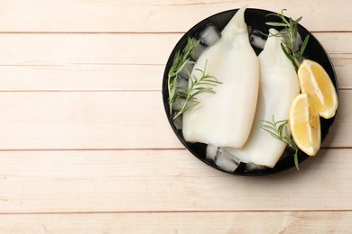 Photo of Pieces of raw squids with ice cubes, lemon and rosemary on light wooden table, top view. Space for text