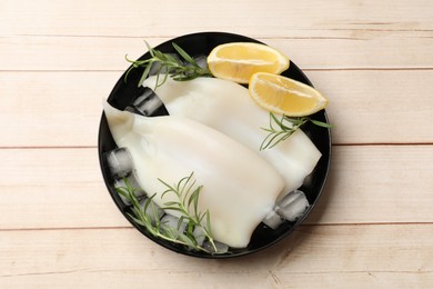 Photo of Pieces of raw squids with ice cubes, lemon and rosemary on light wooden table, top view