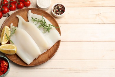 Photo of Pieces of raw squids with products and spices on light wooden table, flat lay. Space for text