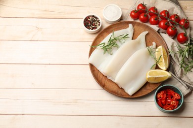 Photo of Pieces of raw squids with products and spices on light wooden table, flat lay. Space for text