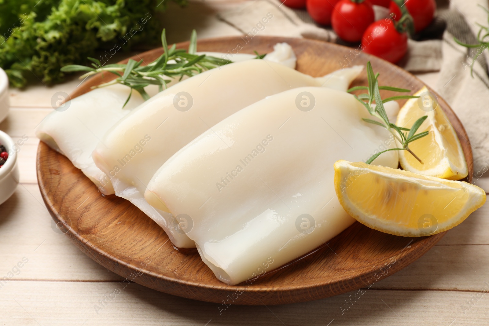 Photo of Pieces of raw squids with lemon and rosemary on light wooden table, closeup