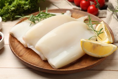 Photo of Pieces of raw squids with lemon and rosemary on light wooden table, closeup