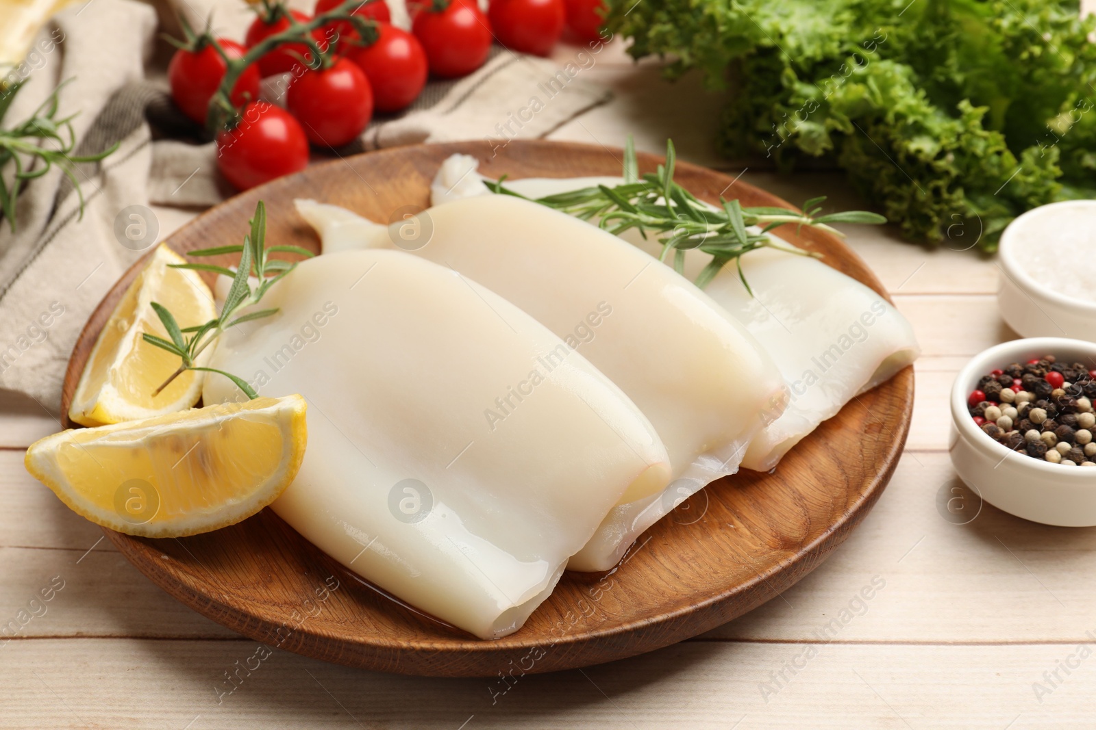 Photo of Pieces of raw squids with lemon and rosemary on light wooden table, closeup
