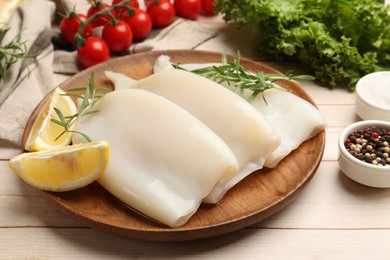 Photo of Pieces of raw squids with lemon and rosemary on light wooden table, closeup