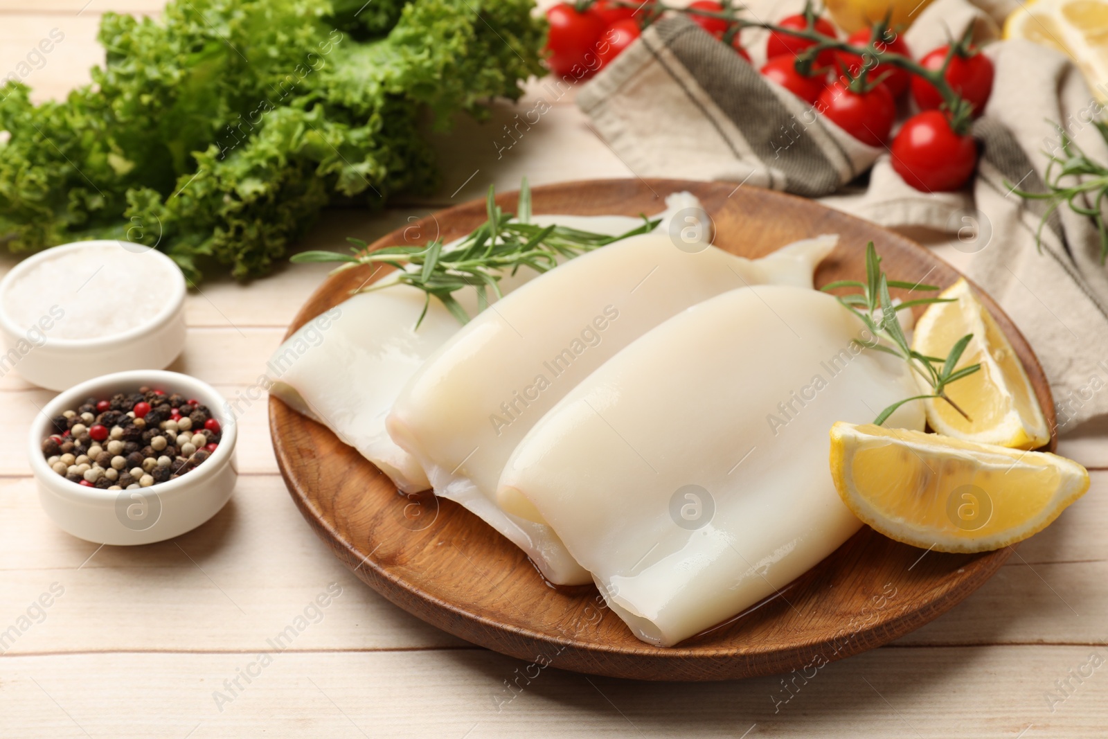 Photo of Pieces of raw squids with products and spices on light wooden table, closeup