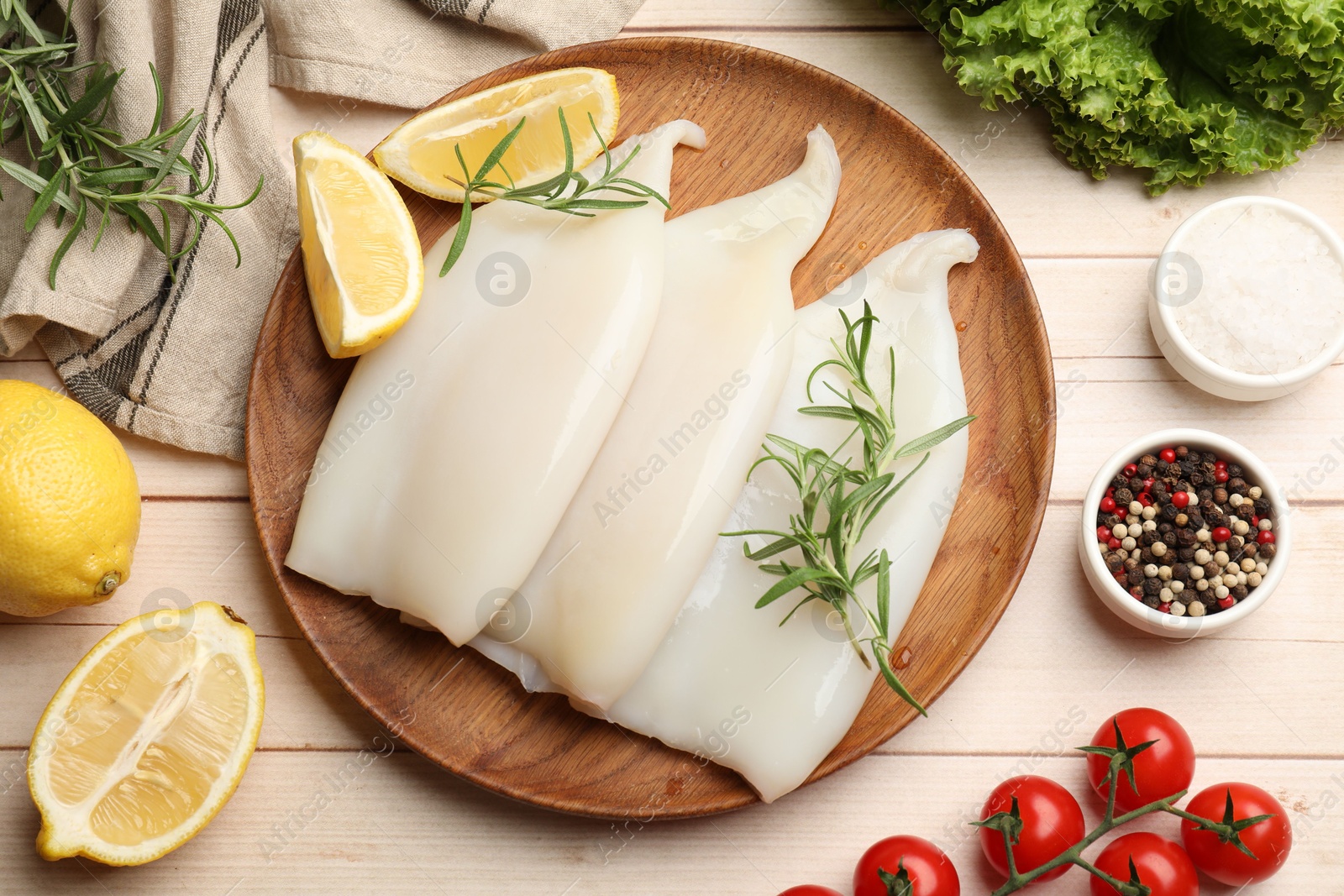 Photo of Pieces of raw squids with products and spices on light wooden table, flat lay