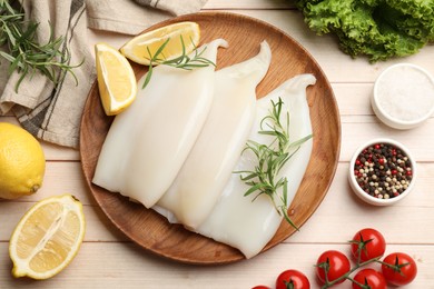 Photo of Pieces of raw squids with products and spices on light wooden table, flat lay