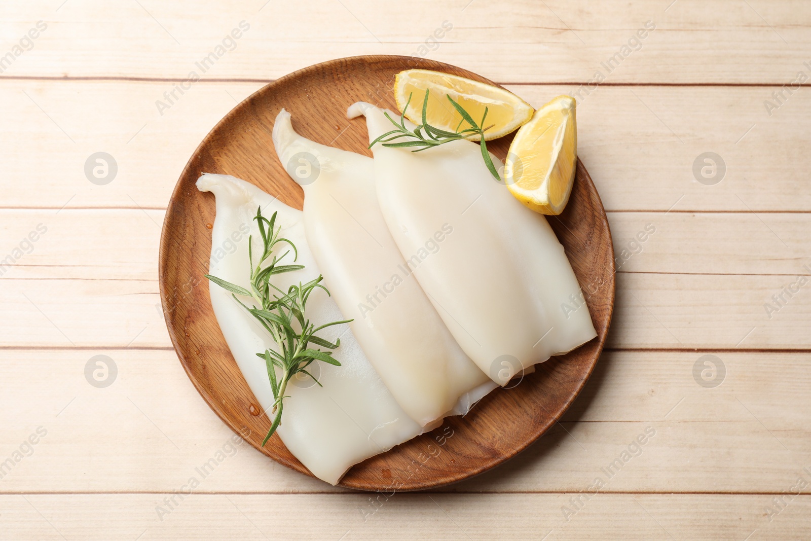 Photo of Pieces of raw squids with lemon and rosemary on light wooden table, top view