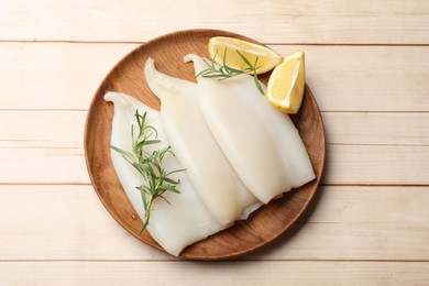 Photo of Pieces of raw squids with lemon and rosemary on light wooden table, top view