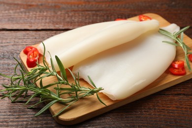 Photo of Pieces of raw squids with rosemary and chili pepper on wooden table, closeup