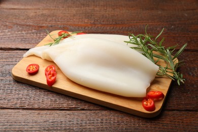 Photo of Pieces of raw squids with rosemary and chili pepper on wooden table, closeup