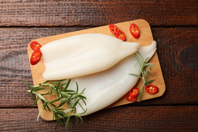 Photo of Pieces of raw squids with rosemary and chili pepper on wooden table, top view