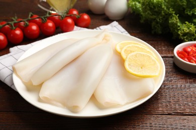 Photo of Pieces of raw squids with lemon on wooden table, closeup