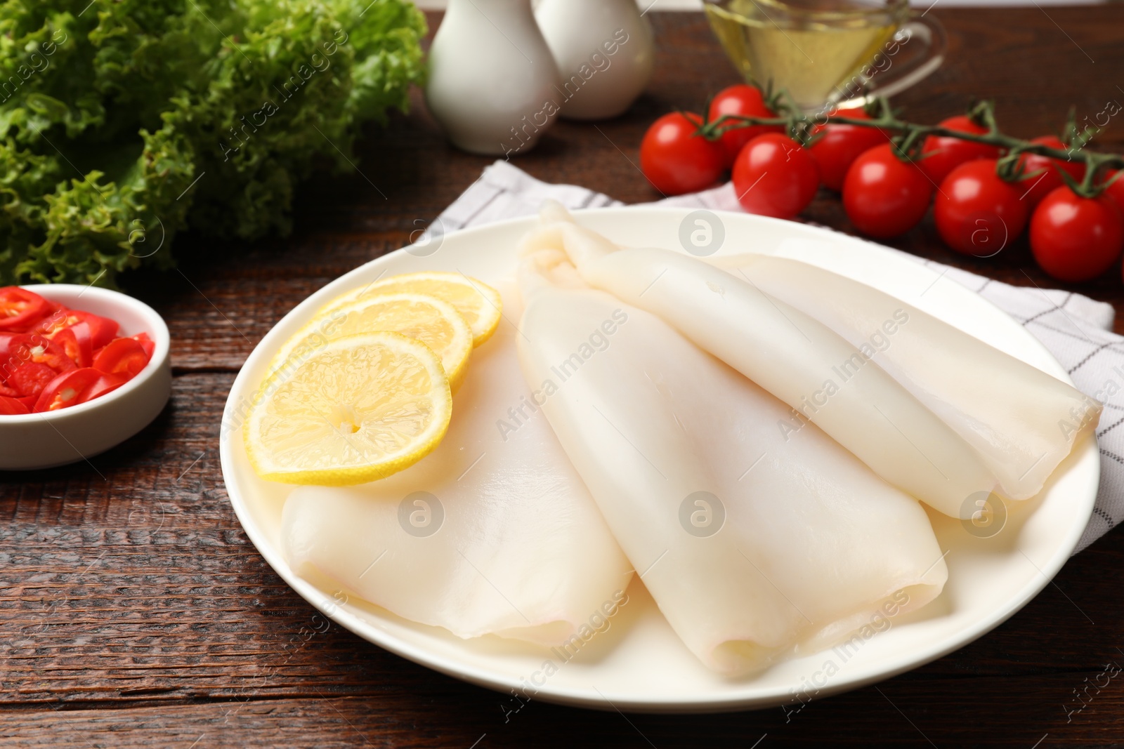 Photo of Pieces of raw squids with lemon on wooden table, closeup