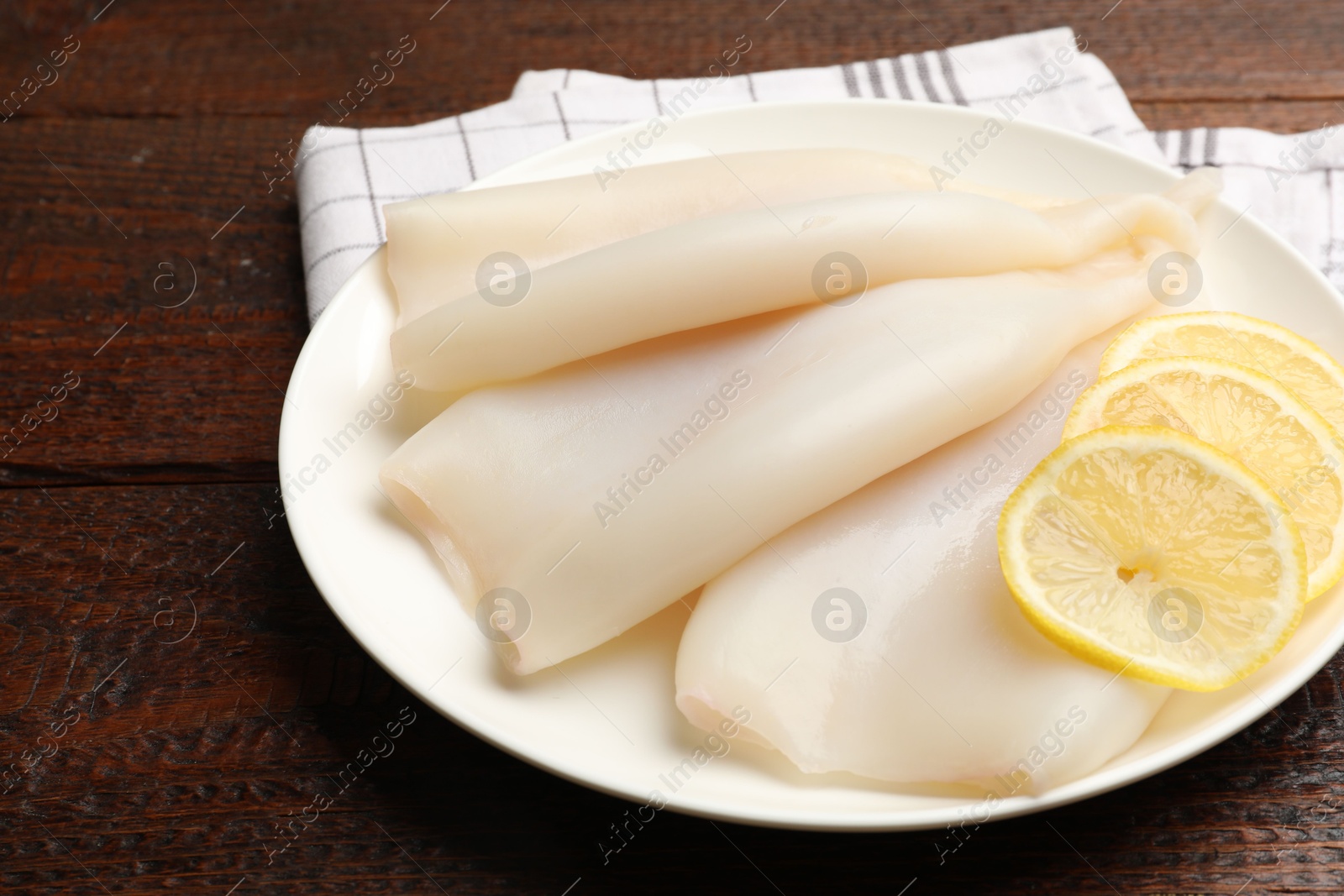Photo of Pieces of raw squids with lemon on wooden table, closeup