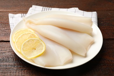 Photo of Pieces of raw squids with lemon on wooden table, closeup