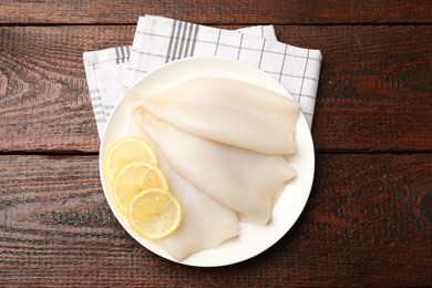Photo of Pieces of raw squids with lemon on wooden table, top view