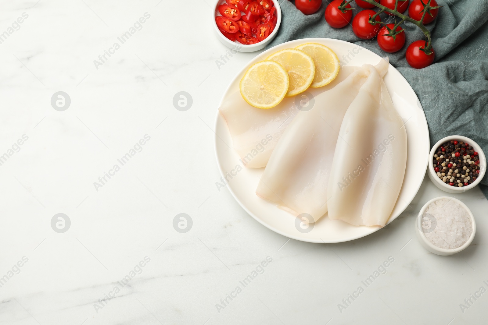 Photo of Pieces of raw squids with lemon, tomatoes and spices on white marble table, flat lay. Space for text