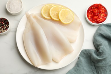 Photo of Pieces of raw squids with lemon and spices on white marble table, flat lay