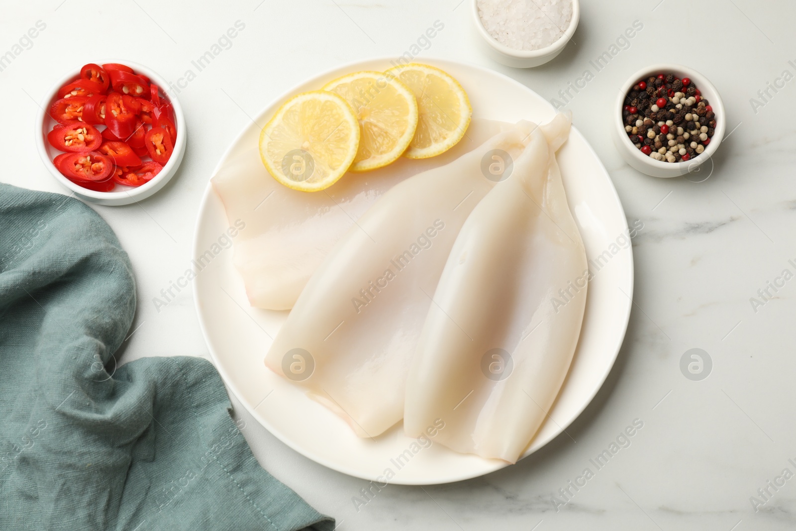 Photo of Pieces of raw squids with lemon and spices on white marble table, flat lay