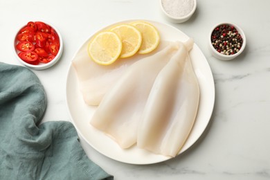 Photo of Pieces of raw squids with lemon and spices on white marble table, flat lay