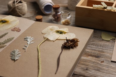 Photo of Dry flowers, leaves and notebook on wooden table, closeup
