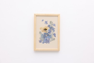 Photo of Beautiful dry flowers and leaves in picture frame on white wall