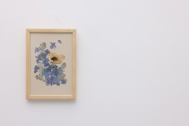 Photo of Beautiful dry flowers and leaves in picture frame on white wall, space for text