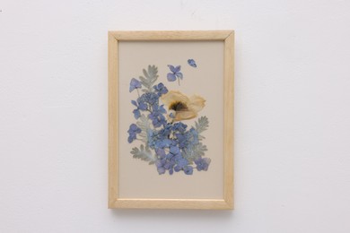 Photo of Beautiful dry flowers and leaves in picture frame on white wall