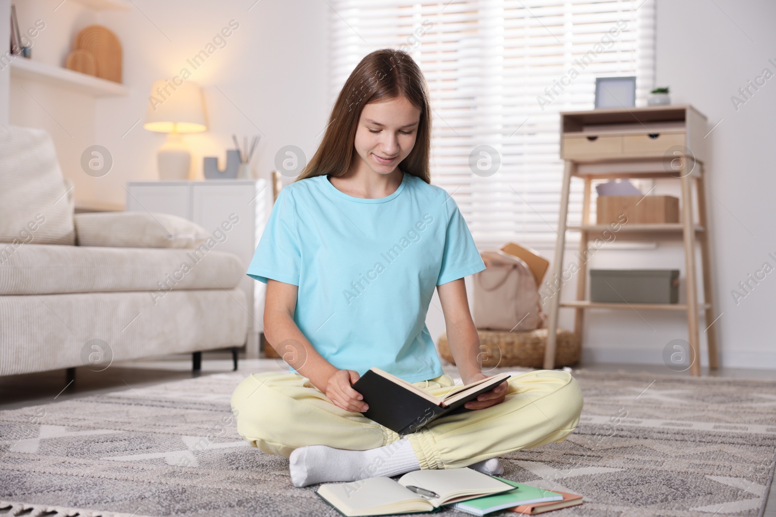Photo of Teenage girl studying with books on floor at home