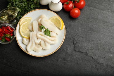 Photo of Raw squid rings, parsley, lemon and other products on dark textured table, flat lay. Space for text
