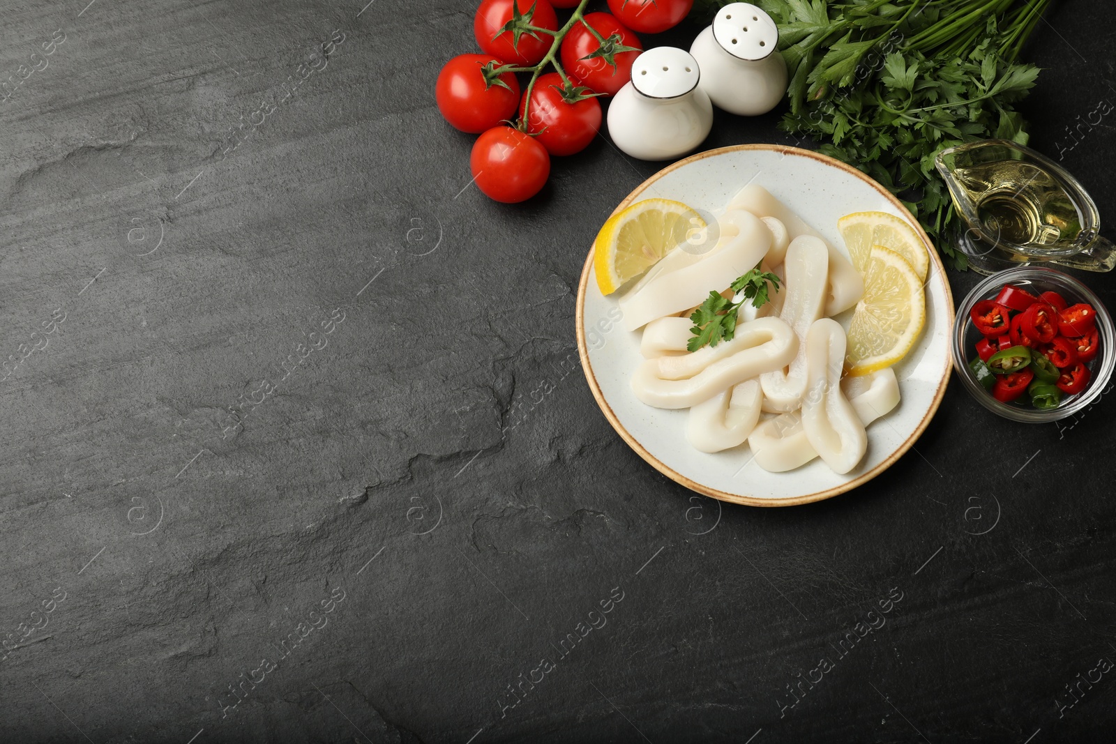 Photo of Raw squid rings, parsley, lemon and other products on dark textured table, flat lay. Space for text