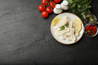 Photo of Raw squid rings, parsley, lemon and other products on dark textured table, flat lay. Space for text