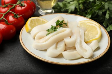 Photo of Raw squid rings, parsley, lemon and tomatoes on dark textured table, closeup