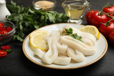 Photo of Raw squid rings, parsley, lemon and other products on dark textured table, closeup