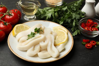 Photo of Raw squid rings, parsley, lemon and other products on dark textured table, closeup