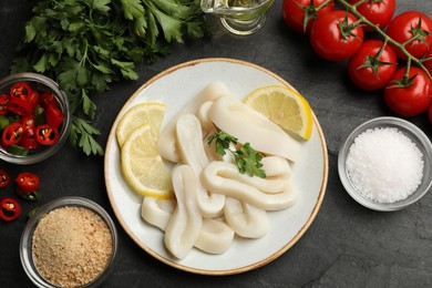Photo of Raw squid rings, parsley, lemon, other products and spices on dark textured table, flat lay