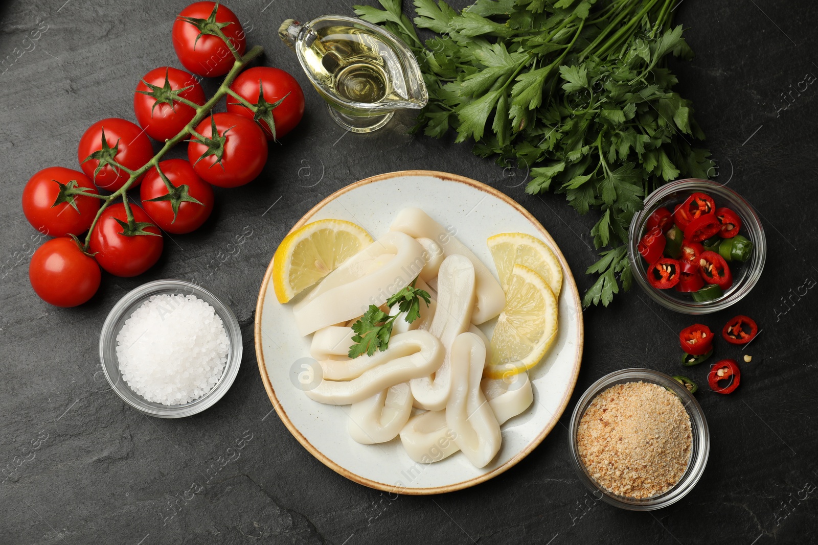 Photo of Raw squid rings, parsley, lemon, other products and spices on dark textured table, flat lay